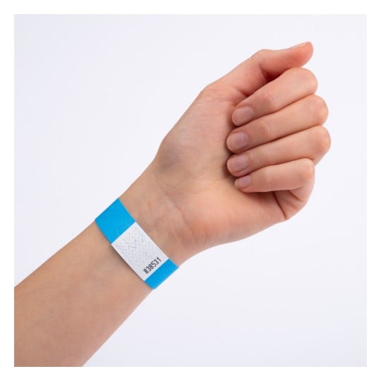 Eine Hand, die ein blau-weißes Armband mit einer Seriennummer trägt, vor einem schlichten Hintergrund gezeigt.