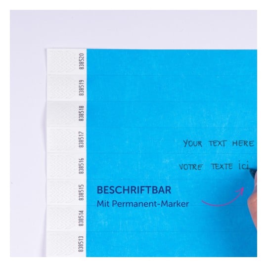 Das Bild zeigt ein blaues Beschriftungsetikett mit Feldern zum Schreiben von Text, beschriftet auf Englisch und Französisch, begleitet von einer Hand, die einen Permanentmarker hält.