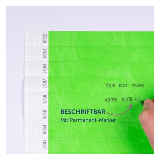 Das Bild zeigt mehrere grüne Haftnotizen mit gedrucktem Text, die darauf hinweisen, dass sie mit einem Permanentmarker beschriftet werden können. Der Text umfasst 'Your Text Here' und 'Votre Texte Ici', zusammen mit einer Hand, die auf einem der Zettel schreibt.