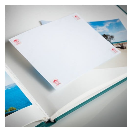 The image shows an open photo album with a blank page and some photos of landscapes. The album has a green spine and the blank page has small labels on the corners.