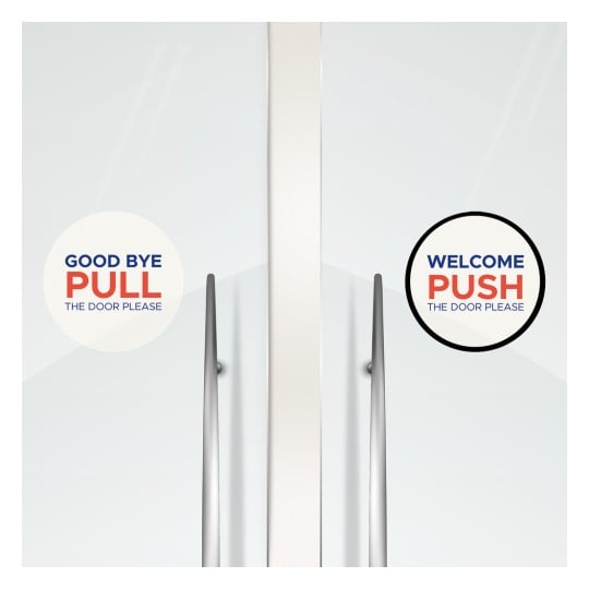 Das Bild zeigt eine Tür mit Schildern, die anweisen, wie sie zu öffnen ist. Auf der einen Seite steht in einem kreisförmigen Design 'GOOD BYE PULL THE DOOR PLEASE', und auf der anderen Seite steht 'WELCOME PUSH THE DOOR PLEASE' ebenfalls in einem kreisförmigen Design.
