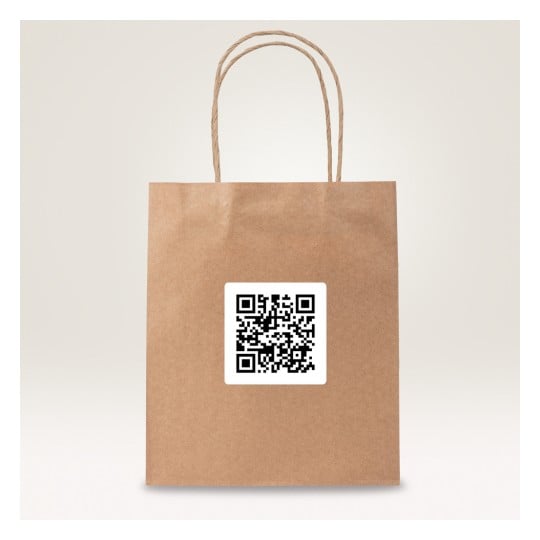 Das Bild zeigt eine braune Papiertüte mit einem QR-Code-Aufkleber darauf. Die Tüte hat zwei gedrehte Papiergriffe und steht vor einem hellen Hintergrund.