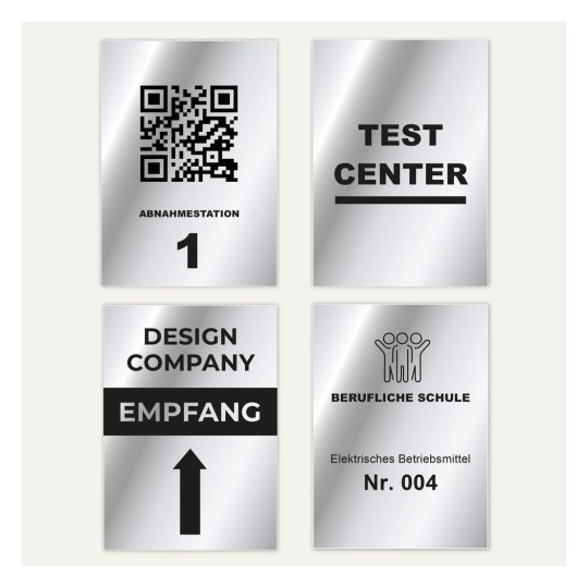Das Bild zeigt vier Schilder mit unterschiedlichen Texten und Symbolen: einen QR-Code mit 'ABNAHMESTATION 1', 'TESTCENTER', 'DESIGN COMPANY EMPFANG' mit einem Pfeil nach oben und 'BERUFLICHE SCHULE' mit einem Symbol und 'Elektrisches Betriebsmittel Nr. 004'.