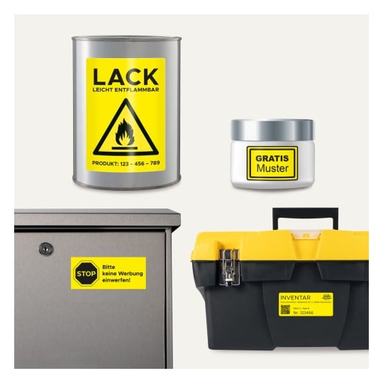 Das Bild zeigt eine silberne Dose mit entzündlicher Farbe und einem Warnhinweis, ein kleines Glas mit einem 'Gratisprobe'-Etikett, eine metallene Box mit einem 'Keine Werbung'-Schild und einen schwarzen Werkzeugkasten mit einem gelben Deckel und einem Inventaretikett.