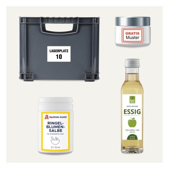 Das Bild zeigt eine graue Aufbewahrungsbox mit der Aufschrift 'LAGERPLATZ 10', ein Glas mit der Aufschrift 'GRATIS Muster', einen Behälter mit Ringelblumensalbe und eine Flasche Apfel-Balsamico-Essig.