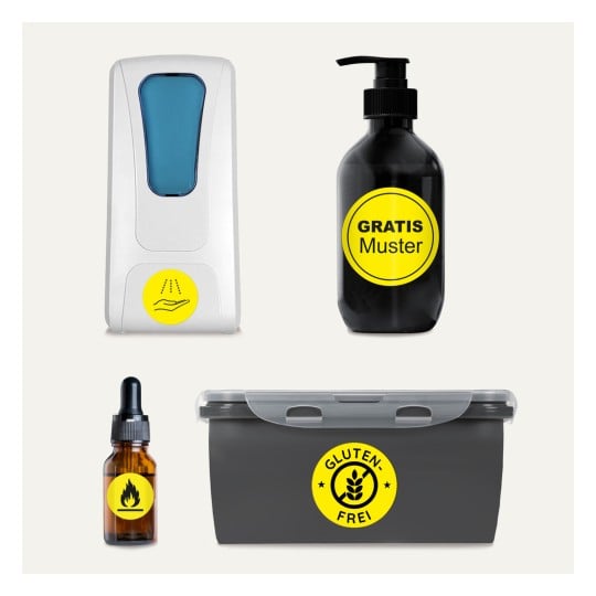 Das Bild zeigt vier Gegenstände: einen weißen Handdesinfektionsmittelspender, eine schwarze Flasche mit der Aufschrift 'Gratis Muster', eine Tropfflasche mit einem Flammensymbol und einen grauen Behälter mit der Aufschrift 'Gluten Frei'. Jedes Objekt hat ein auffälliges gelbes rundes Etikett.
