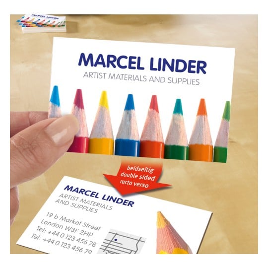 Das Bild zeigt eine Visitenkarte für Marcel Linder, die Künstlerbedarf und -materialien präsentiert. Die Karte ist bunt und zeigt oben Stifte. Sie enthält auch Kontaktinformationen und gibt an, dass sie beidseitig bedruckt ist.