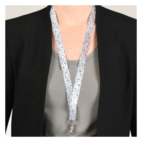 Das Bild zeigt eine Person, die einen schwarzen Blazer über einem grauen Hemd trägt, mit einem bunten, floralen Schlüsselband um den Hals, das einen Ausweis hält.