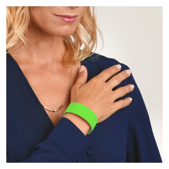 Das Bild zeigt eine Frau, die eine marineblaue Bluse und ein grünes Armband an ihrer Hand trägt. Sie hält ihre Hand an ihre Schulter, und ihr Haar ist in lockeren Wellen gestylt. Der Hintergrund ist ein leichter Farbverlauf.