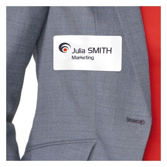 Das Bild zeigt eine Person, die eine graue Anzugsjacke trägt, an der ein Namensschild mit der Aufschrift 'Julia SMITH Marketing' befestigt ist.