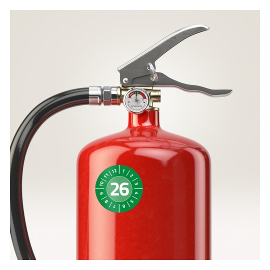 Das Bild zeigt eine Nahaufnahme eines roten Feuerlöschers. Der Feuerlöscher ist mit einem Griff und einer Düse ausgestattet, sowie einem Druckmesser oben, der den Status anzeigt. Auf dem Körper befindet sich ein grünes rundes Etikett mit der Nummer 26.