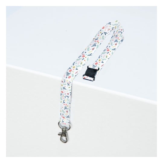 Das Bild zeigt ein gemustertes Schlüsselband mit Blumendesigns und einem Metallclip, das auf einer hellen Oberfläche liegt.