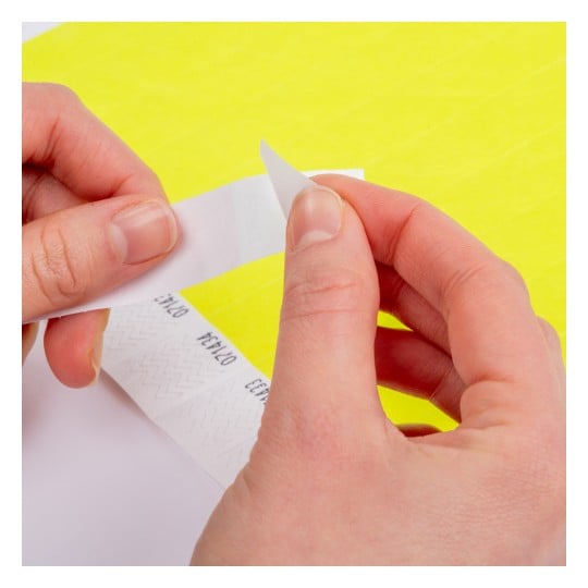 Das Bild zeigt die Hände einer Person, die einen Papier- oder Aufkleberstreifen von einem Blatt abziehen, mit einem leuchtend gelben Hintergrund und gedruckten Designs auf dem Streifen.