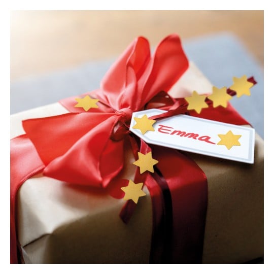 Das Bild zeigt ein schön verpacktes Geschenk mit einem roten Band und goldenen Sternverzierungen. Ein Anhänger mit dem Namen 'Emma' ist an dem Geschenk befestigt und verleiht ihm eine persönliche Note.