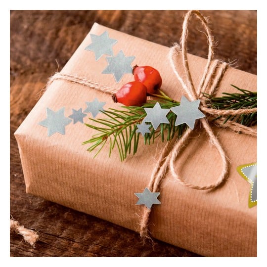 Das Bild zeigt ein wunderschön verpacktes Geschenk in braunem Papier, verziert mit einem natürlichen Kordelbogen, grünen Blättern, roten Beeren und blauen sternförmigen Ausschnitten.