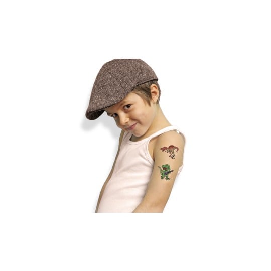 Ein Kind, das eine Schiebermütze und ein weißes Tanktop trägt, lächelt, während es zwei bunte temporäre Tattoos auf seinem Arm präsentiert. Die Tattoos zeigen einen Dinosaurier, der Fußball spielt, und einen weiteren Dinosaurier, der Gitarre spielt.