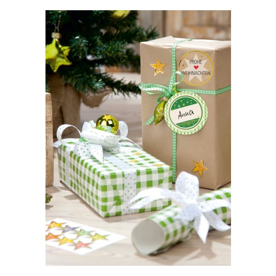 Das Bild zeigt Weihnachtsgeschenke, die in dekoratives Papier eingewickelt sind, mit einem kleinen Weihnachtsbaum im Hintergrund. Die Geschenke haben grüne und weiße Muster, und eines ist mit "Anna" beschriftet. Es gibt goldene Verzierungen und einen Stern auf den Geschenken, die eine festliche Atmosphäre schaffen.
