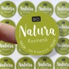 Das Bild zeigt einen runden Logosticker mit Aufschrift Natura, der auf einem Finger klebt.