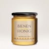 Ein Honigglas auf dem ein Etikett aus Bagasse-Papier klebt, wo auf dem BIENENHONIG und ein schlichtes Design zu sehen ist.