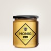 Ein Honigglas mit einem goldenen Etikett in Rautenform auf dem "HONIG" steht.