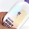 Auf einem Body Lotion Behältnis klebt ein bedruckter Aufkleber aus Perlmutt-Folie. Auf dem Aufkleber steht "aura Body Lotion" und eine Blume ist abgebildet. Der Fokus des Bildes liegt auf dem Material des Aufklebers.
