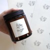 Im Vordergrund hält eine Hand ein Glasbehältnis auf dem ein bedruckter Aufkleber aus Perlmutt Folie klebt. Im Hintergrund sieht man die Aufkleber auf verschiedenen Bögen.