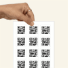 Eine Hand hält einen Bogne mit QR Code Aufklebern.