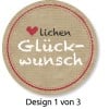 Das Bild zeigt ein kreisförmiges Design mit einem hellbraunen Hintergrund, der an Pappe erinnert. Es enthält das Wort 'Glückwunsch' in einer weißen, spielerischen Schrift, begleitet von einem Herz und dem Wort 'lichen' in einer stilvollen schwarzen Schrift. Es ist als 'Design 1 von 3' gekennzeichnet.