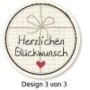 Das Bild zeigt ein kreisförmiges Design mit einem Rasterhintergrund, eine Schleife aus Schnur und den Text 'Herzlichen Glückwunsch'. Es enthält auch ein kleines Herz und gibt an 'Design 3 von 3'.