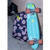 Ein türkisfarbenes Skateboard lehnt an einem gemusterten Rucksack mit Fruchtmotiven.