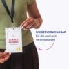 Oberkörper einer Person, die ein grünes Oberteil und ein schwarzes Schlüsselband trägt und einen weißen Ausweishalter hält?