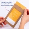 Das Bild zeigt eine Person, die einen Rahmen aus braunem Papier mit einer gelben Karte darin hält. Der sichtbare Text umfasst 'Coralie Miaping' und Informationen über das Material, die darauf hinweisen, dass es sich um nachhaltiges Papier handelt. Auch die Abmessungen sind angegeben.