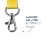 Das Bild zeigt einen metallischen Karabiner, der an einem gelben Riemen befestigt ist, mit einem deutschen Text, der seine Verwendung zur Befestigung von Namensschildern oder Zubehör erklärt.