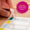 Eine Hand zieht eine transparente Folie von einem Etikettenbogen auf einer Holzoberfläche ab, mit einem Text, der einen Schritt im Etikettierungsprozess anzeigt.