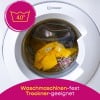 Das Bild zeigt eine Draufsicht einer Waschmaschine mit einer transparenten Tür, in der sich ein gelbes T-Shirt und ein gemustertes Gewebe befinden. Es gibt ein Etikett mit einer Waschanleitung von 40 Grad Celsius, zusammen mit Text, der besagt, dass die Artikel für Waschmaschinen und Trockner geeignet sind.