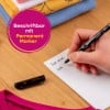 Das Bild zeigt eine Person, die mit einem Permanentmarker auf einem Etikettenbogen schreibt, während im Hintergrund auf einer Holzoberfläche gefaltete Kleidung in verschiedenen Farben gestapelt ist.