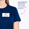 Das Bild zeigt eine Person, die ein marineblaues T-Shirt mit einem Namensschild trägt, auf dem "B. Carlos, MARKETING DIRECTOR" steht. Der begleitende Text zum Bild ist auf Deutsch und erwähnt hochwertige Textilfolie und eine weiche Haptik, die sich der Kleidung anpasst.