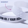 Das Bild zeigt zwei weiße Armbänder. Eines trägt den Text 'WASSERFEST,' und das andere hat 'DESIGN ICI / YOUR DESIGN' in Schwarz aufgedruckt. Die Armbänder haben unterschiedliche Texturen, darunter eine glatte Oberfläche und eine mit einem erhabenen Punktmuster.