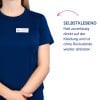 Das Bild zeigt eine Frau, die ein dunkelblaues T-Shirt trägt, mit einem Namensschild, auf dem 'B. Carlos Marketing Director' steht. Daneben gibt es einen deutschen Text, der darauf hinweist, dass das Etikett selbstklebend ist, zuverlässig auf Kleidung haftet und ohne Rückstände entfernt werden kann.