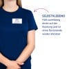 Das Bild zeigt eine Person, die ein dunkelblaues Hemd trägt, mit einem Namensschild, auf dem 'B. Carlos, Marketing Director' steht. Es gibt einen Textabschnitt, der die selbstklebende Eigenschaft des Namensschilds hervorhebt und besagt, dass es zuverlässig auf Kleidung haftet und rückstandsfrei entfernt werden kann.