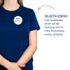 Das Bild zeigt eine Person, die ein marineblaues T-Shirt trägt, mit einem runden Abzeichen, das einen Namen und einen Titel anzeigt. Der Text neben der Person beschreibt ein selbstklebendes Produkt, das an Kleidung haftet und ohne Rückstände entfernt werden kann.