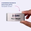 Das Bild zeigt ein Namensschild von Avery mit dem Namen 'Paul Meyer'. Es hat eine Edelstahloptik und Abmessungen von 80 x 34 mm. Eine Hand hält das Schild, und zusätzlicher Text hebt die Anzahl der Schilder in der Verpackung hervor.