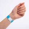 Eine Hand, die ein blau-weißes Armband mit einer Seriennummer trägt, vor einem schlichten Hintergrund gezeigt.