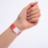 Das Bild zeigt eine Hand, die ein rotes Armband mit einem Zickzackmuster und einem kleinen aufgedruckten Etikett trägt, was darauf hindeutet, dass es möglicherweise zu Identifikationszwecken verwendet wird.
