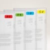 Das Bild zeigt eine Reihe von transparenten Plastikmappen, die nebeneinander angeordnet sind, jede mit einer Beschriftung, die auf Abschnitte hinweist, die nach Buchstabenbereichen organisiert sind: A-D in Rot, E-H in Grün, I-R in Blau und S-Z in Gelb. Sie enthalten gedruckte Dokumente, obwohl der Text teilweise verdeckt ist.