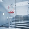 Das Bild zeigt eine Treppe mit einer Glastür neben einem Schild, das die Benutzer anweist zu drücken. Das Schild weist darauf hin, dass es antimikrobielle Oberflächen aufweist und hebt die Sicherheit hervor.