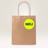 Das Bild zeigt eine braune Papiereinkaufstüte mit einem kreisförmigen neon-gelben Etikett, auf dem in schwarzer Schrift das Wort 'NEU' steht.