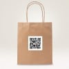 Das Bild zeigt eine braune Papiertüte mit einem QR-Code-Aufkleber darauf. Die Tüte hat zwei gedrehte Papiergriffe und steht vor einem hellen Hintergrund.