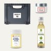 Das Bild zeigt eine graue Aufbewahrungsbox mit der Aufschrift 'LAGERPLATZ 10', ein Glas mit der Aufschrift 'GRATIS Muster', einen Behälter mit Ringelblumensalbe und eine Flasche Apfel-Balsamico-Essig.