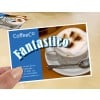 Das Bild zeigt eine Werbekarte eines Cafés, auf der ein Cappuccino mit Schaum und Kakaopulver abgebildet ist. Die Karte enthält den Namen "CoffeeCo" und das Wort "Fantastico" in prominenter Darstellung. Kontaktinformationen und eine Website sind ebenfalls sichtbar.
